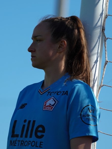 Joueuse en maillot bleu de profil près du poteau de but, ciel dégagé
