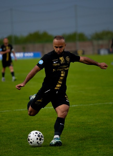 Joueur en maillot noir et or frappant le ballon en pleine extension